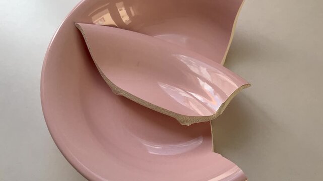 Pink ceramic plate breaking apart and shattering into pieces representing fragility, domestic accident, relationship breakup, and the concept of imperfection and repair