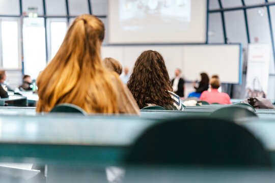 A large group of diverse people attending a professional presentation or educational workshop in a modern lecture hall. Focus on the audience from behind.