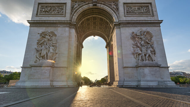 View of the Arc de Triomphe with intricate stone sculptures and the sun shining through the arch in Paris, Ile-de-France, France.