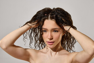Fototapeta premium Woman massaging wet curly hair roots during moisturizing hair care routine. Concept of curl definition, scalp care, hydration treatment, beauty tutorial and natural haircare content.