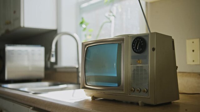 Slow pan over a small black-and-white tube TV with no signal static on a scratched formica kitchen counter with peeling paint and aged cabinets.