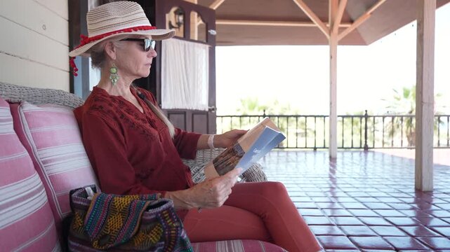 Mature woman sits on a terrace in Santa Rosalia looking at a travel guide and enjoying the views of Baja California Sur.