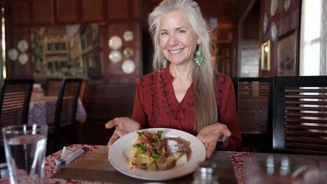 Mature woman sits at a table and smiles as she admires her food in Santa Rosalia, Baja California, during her travel experience.