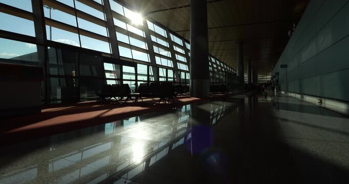 Low angle view of empty airport terminal as bright sun rays cast long shadows and reflections across polished floor with sunlight flashing through windows. Slow motion forward glide shot.