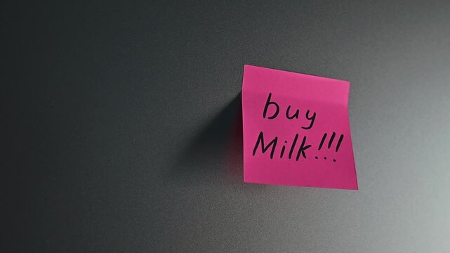 A sticky note with a shopping reminder is attached to a wall in an indoor location. The note emphasizes the importance of buying milk, showcasing a common task that many people need to remember