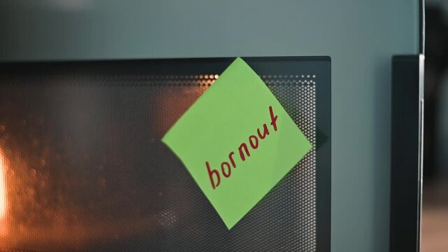 A person reaches for a microwave that has a sticky note labeled burnout attached to its door. The setting appears to be a kitchen, highlighting everyday life and interactions with kitchen appliances