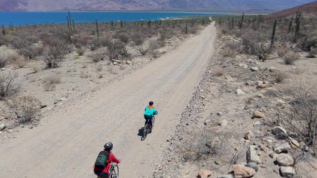 Mature man and woman enjoy biking together on a dirt road in Bahia de Los Angeles Baja California Mexico surrounded by nature.