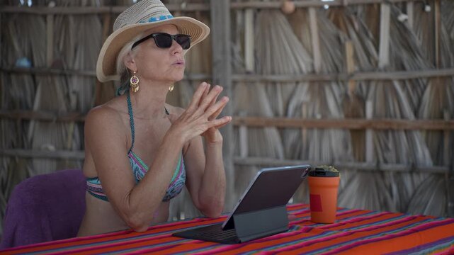 A mature woman is excited as she uses a computer tablet on a tropical beach while on vacation.