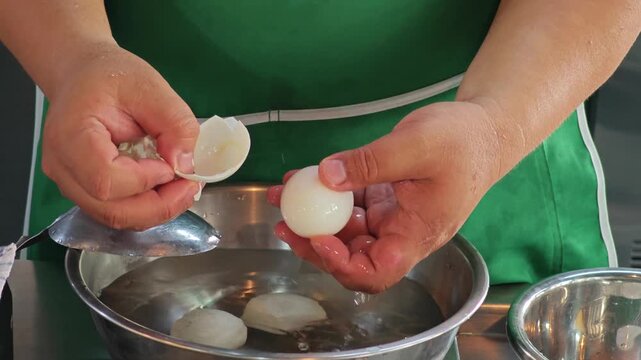 Close-up of chef hands peeling a hard-boiled egg over a metal bowl.