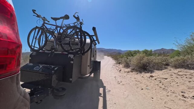 A teardrop camper trailer is towed by an SUV on a sandy road in Baja California while looking for a campsite in the desert.