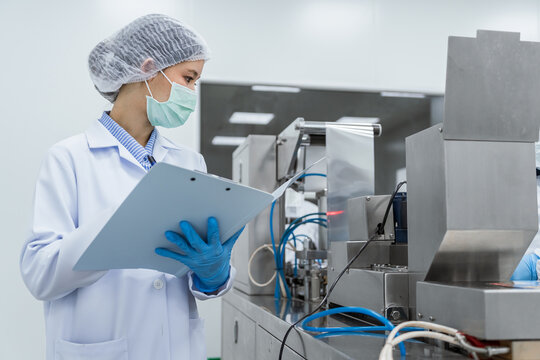 Clean food factory worker inspects production line with cli. Quality control inspector and factory workers operating automated packaging machinery in a sterile pharmaceutical manufacturing facility.