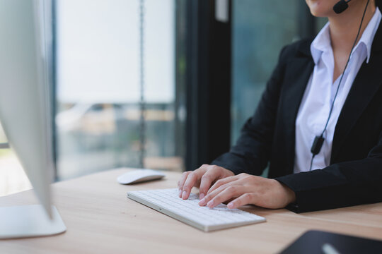 Customer support representative typing on a keyboard, wearing a headset, assisting clients with inquiries and providing online help and dedicated solutions in a modern office setup