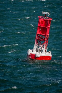 View of a red navigational buoy covered in ice floating in the choppy blue waters of Martha's Vineyard in Edgartown, Massachusetts, United States.