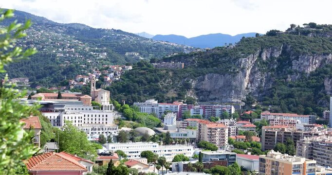 Scenic Nice city panorama with Cimiez Monastery church tower and mountain range background. French Riviera urban landscape from hill viewpoint with olive tree branch on foreground and traditional red