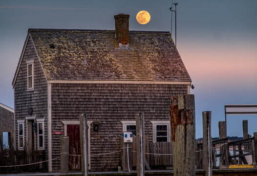 View of Martha's Vineyard featuring a weathered shingle building with a full moon rising behind the chimney at twilight in Edgartown, Massachusetts, United States.