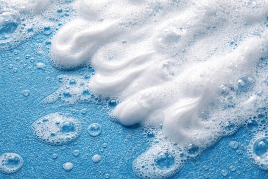 White foam lather of cleanser gel and shaving cream bubbles on blue textured surface