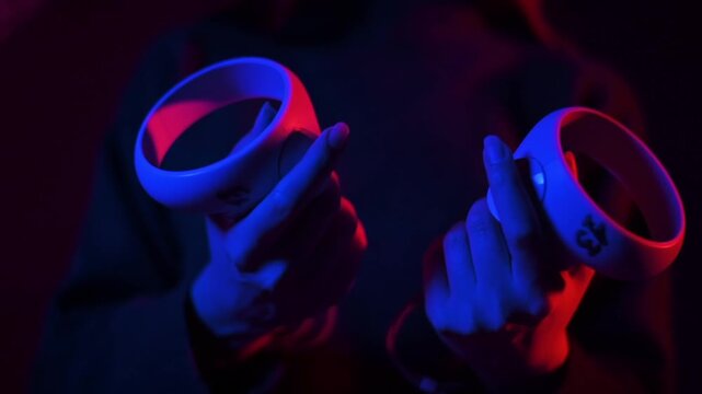 Person holding virtual reality controllers in a dark room with neon red and blue lighting effect.