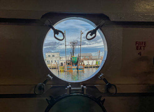View of a fishing boat docked in the harbor seen through a circular ship porthole under a cloudy sky in Edgartown, Massachusetts, United States.