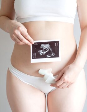 Pregnant woman holding sonogram image with medical device