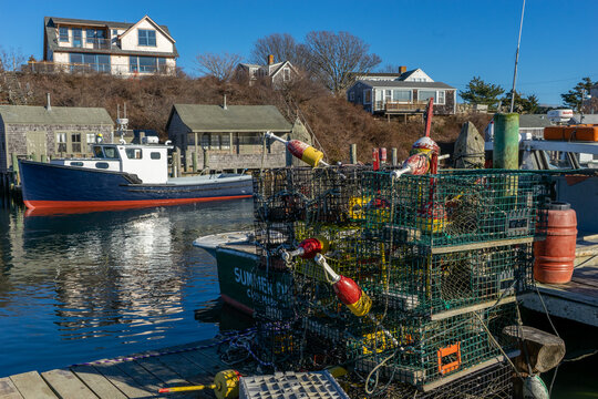 View of fishing boats and stacked lobster traps on a wooden dock with coastal houses in the background at Martha's Vineyard Edgartown, Massachusetts, United States.