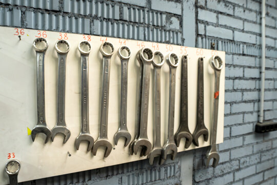 Organized set of professional wrenches and sockets on a tool board in an auto repair shop. Mechanical tools hanging on a white wall organizer in a garage with industrial brick background.