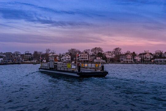 View of the Chappaquiddick ferry crossing the harbor with coastal houses and a twilight sky in Edgartown, Massachusetts, United States.
