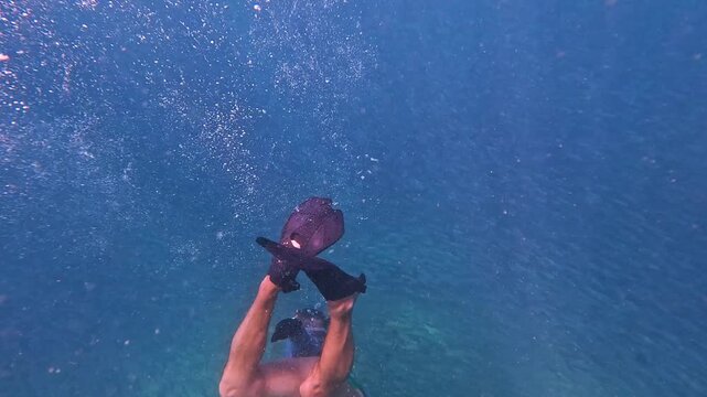 A person dives and swims among a huge school of fish in the clear blue ocean, exploring the diverse marine life of a coral reef during the day