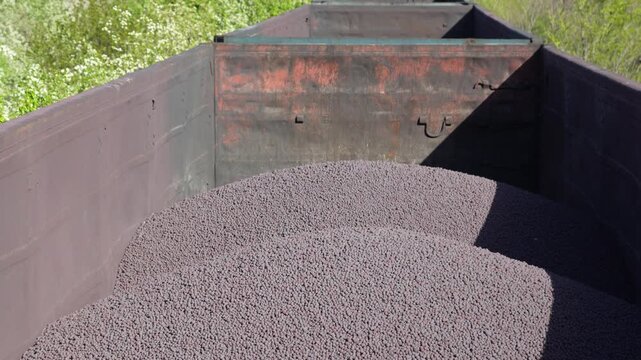 Open freight train wagons loaded with metal pellets or iron ore balls moving along industrial railway tracks. Heavy industry transportation and mining logistics concept.