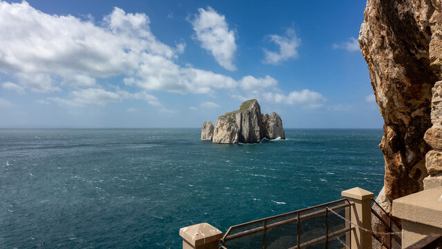 View of Scoglio Pan di zucchero sea stack rising from the Mediterranean sea under a blue sky with white clouds in Masua, Sardegna, Italy.