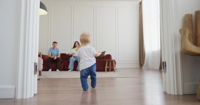 Toddler taking first steps toward smiling mother in a bright modern living room, capturing a warm family milestone at home