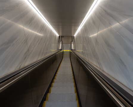 View of a modern subway escalator descending between polished marble walls with bright linear lighting in New York, New York, United States.