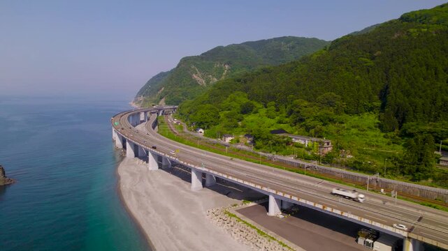山肌に沿う北陸自動車道のダイナミックなカーブ 走行車両を追従して前進する空撮