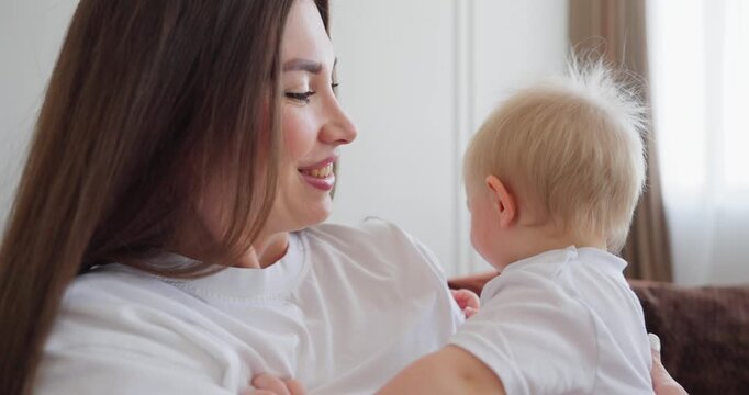 Young mother cuddling and playing with her smiling baby on a cozy sofa in a bright living room, sharing tender family bonding at home