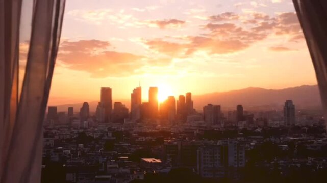 Stunning sunset over metropolitan skyline viewed through flowing white curtains during golden hour featuring silhouetted skyscrapers under warm orange clouds.