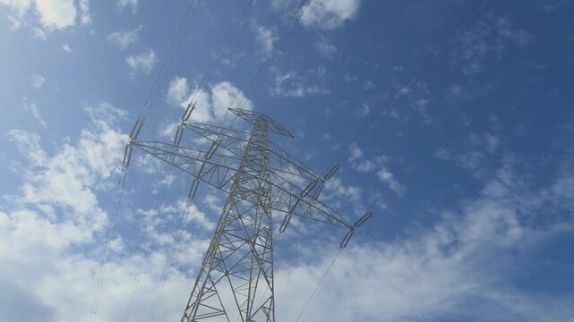 Electricity pylon with high voltage power lines for energy transmission and distribution standing against a blue sky with white clouds on a sunny day in the background