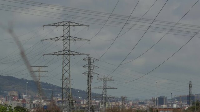 High voltage power lines and electrical transmission towers connecting an urban industrial area with the city of barcelona, spain, under a cloudy and polluted sky