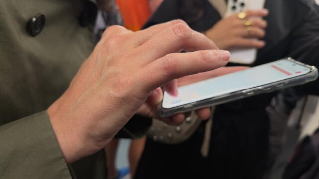 Person using a smartphone in a crowded public space, scrolling and typing on the touch screen with their finger while commuting on the subway or waiting for a bus