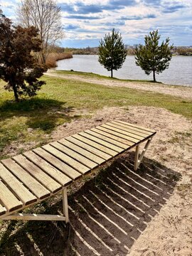 A rustic wooden sunbed on a sandy beach by a calm lake