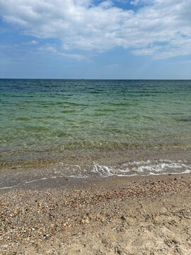 Crystal Clear Turquoise Sea Water on a Sandy Pebble Beach Under Blue Sky