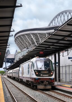 Seattle, Washington - June 22, 2025: An Amtrak Cascades passenger train at the King Street Station platform. Lumen Field, a major sports stadium, is visible in the background