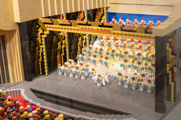 Obraz premium A stage scene made of Lego blocks shows many small figures performing. The setting includes an audience watching the show. Bright colors fill the scene