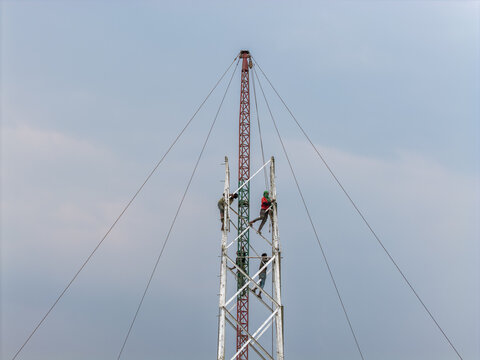 Trishal Upazila, Bangladesh - 13 May 2026: Aerial view of workers climbing a tall telecommunications tower structure under a clear sky.