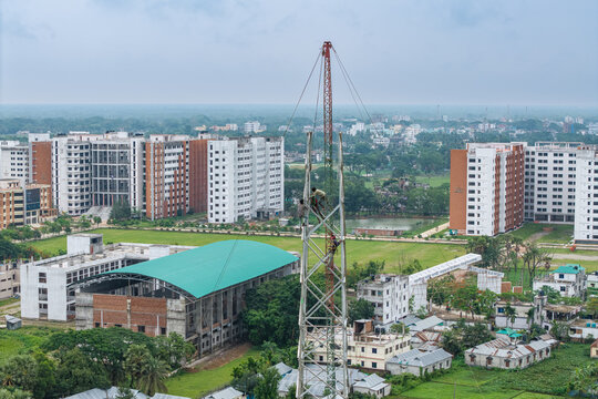 Trishal Upazila, Bangladesh - 13 May 2026: Aerial view of workers climbing a tall metal tower on a university campus with modern buildings and green landscapes.