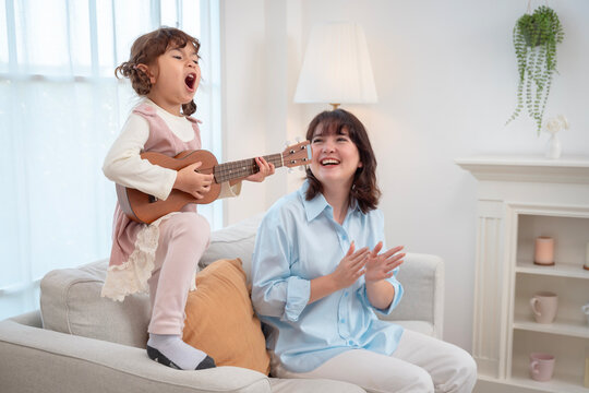 Little girl playing ukulele and singing passionately with her mother