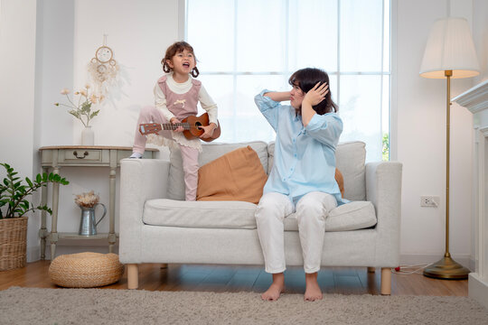 Little girl playing ukulele and singing passionately with her mother