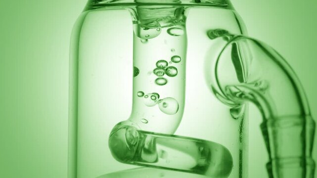 Pure transparent solution flowing through a glass tube, causing bubbles to condense and chaotically move inside it on green ramp background