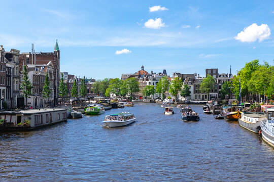Busy Amstel River with Tour Boats and Historic Dutch Buildings in Amsterdam Summer