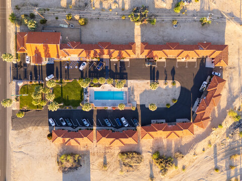 Twentynine Palms, United States - 07 April 2026: Aerial view of El Rancho Dolores Motel featuring a central swimming pool, palm trees, and parked cars in the desert landscape.