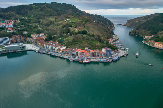Pasai Donibane, Spain - 10 March 2026: Aerial view of the Harbour mouth of Pasaia with colorful waterfront buildings, docked boats, and lush green hills under a cloudy sky.