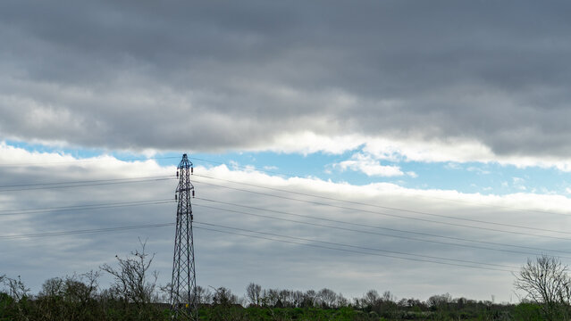 A power line tower against a backdrop of a cloudy sky split by a patch of blue sky